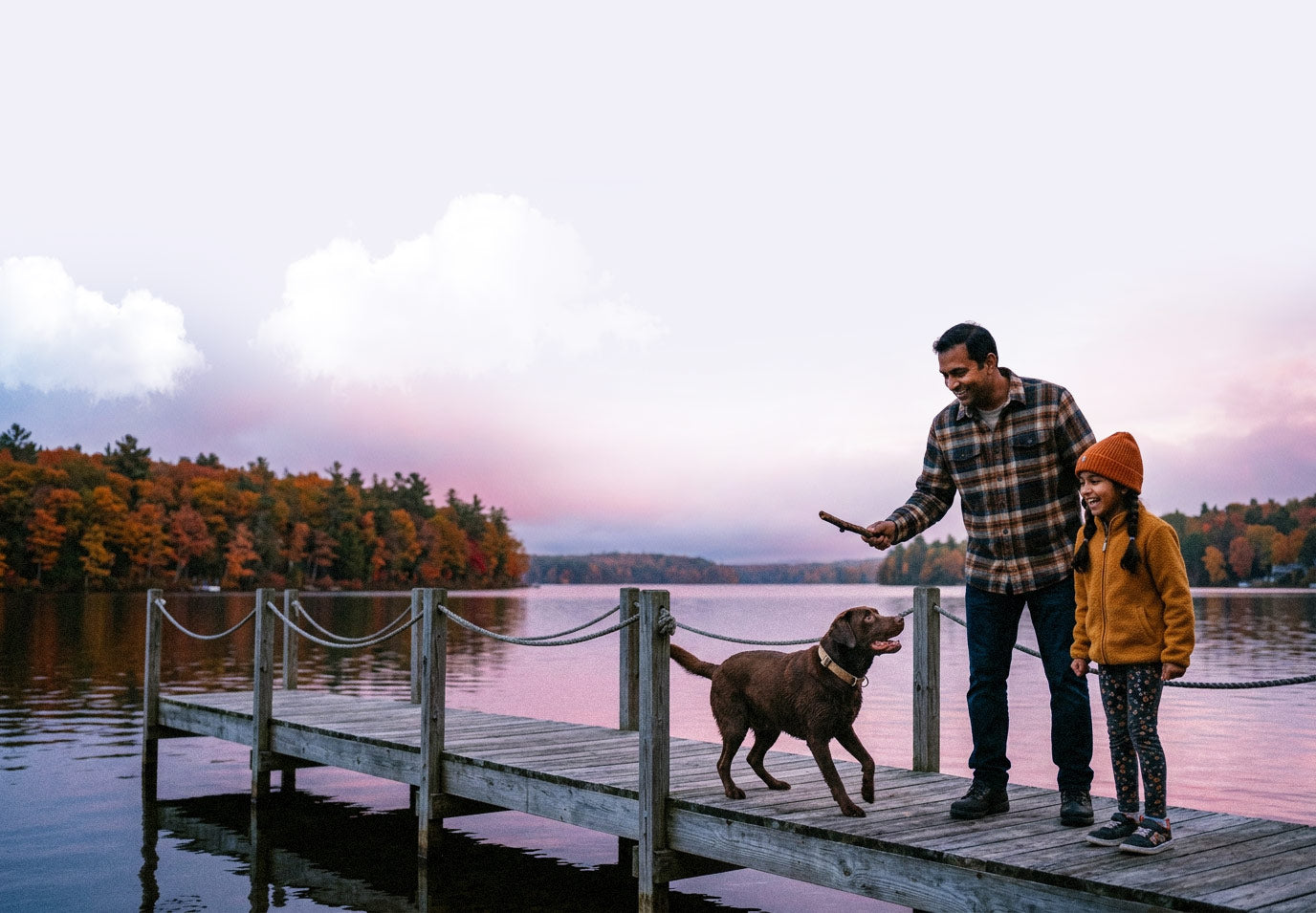 Man and child with a dog on a dock by a lake at sunset