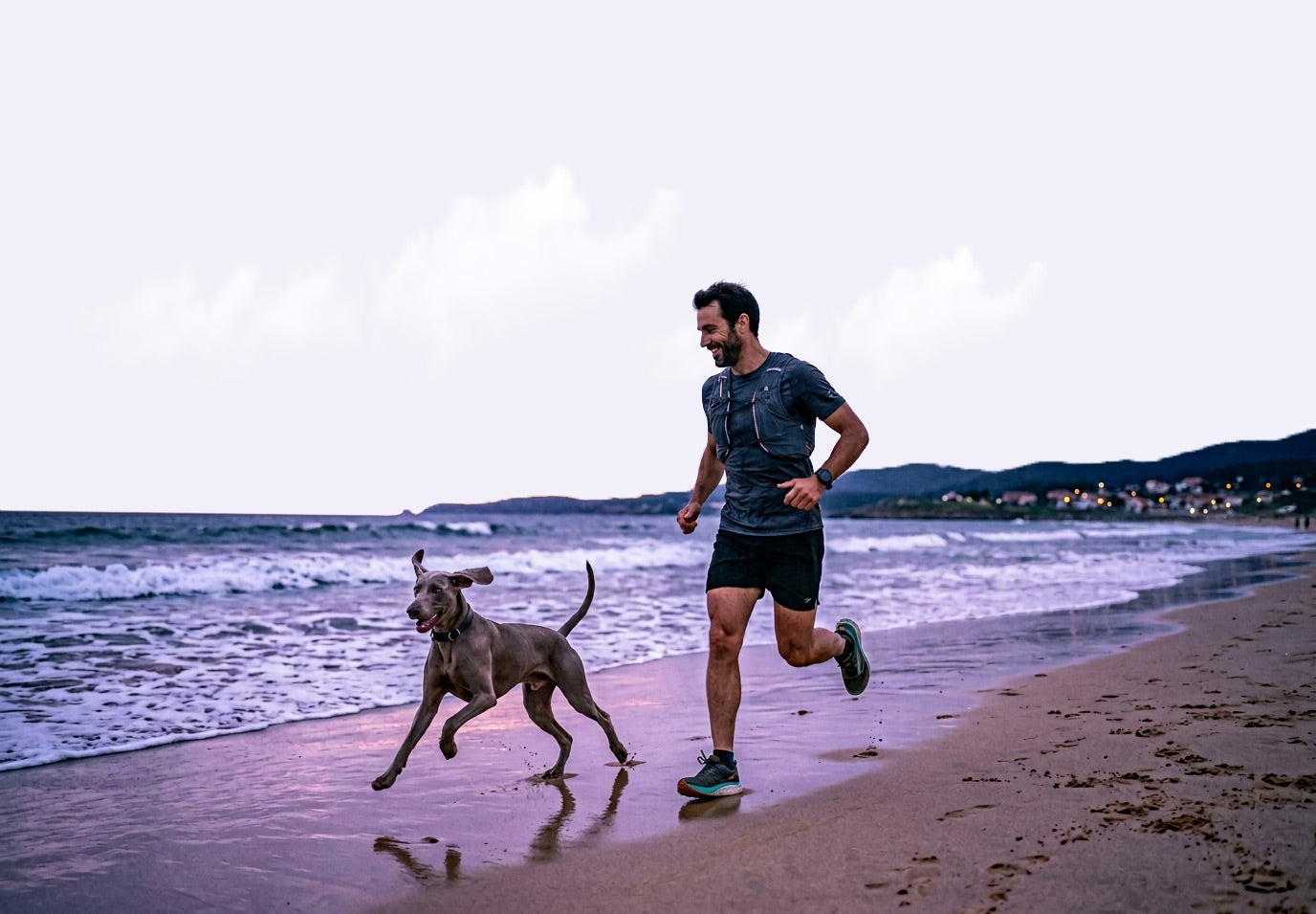 Man running on a beach with a dog at sunset