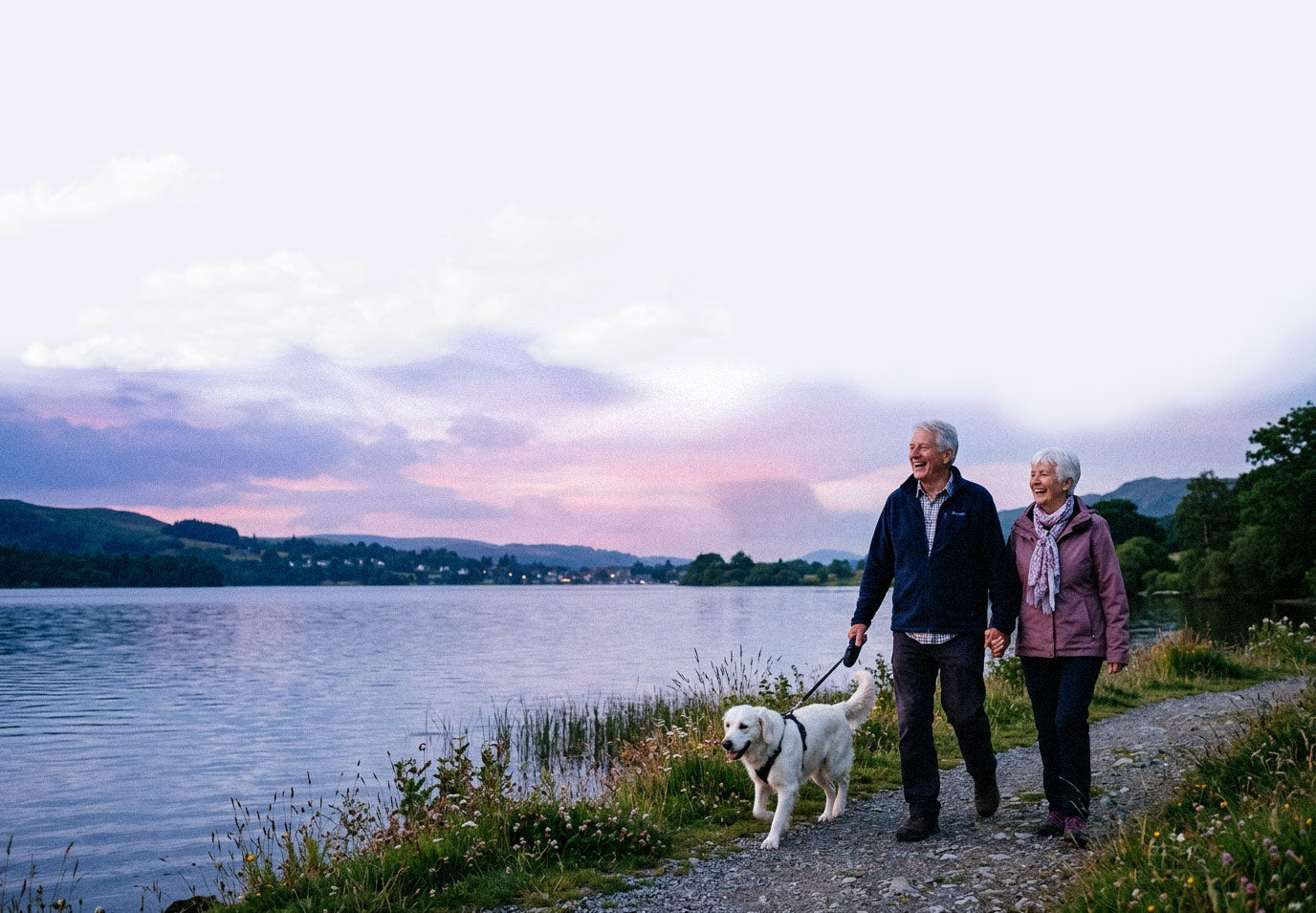 Senior couple walking a dog by a lake at sunset