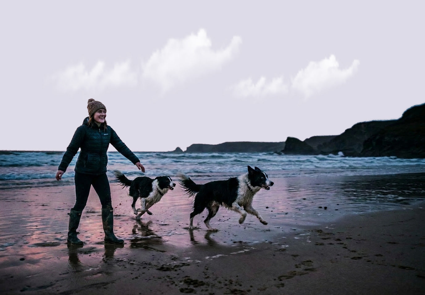 Woman walking two dogs on a beach with a cloudy sky