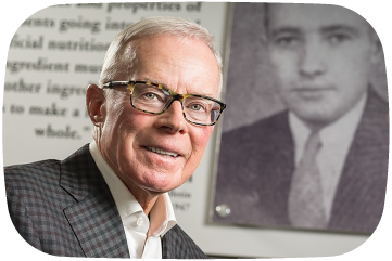 Man in glasses and suit in front of a black and white photo of another man with text overlay