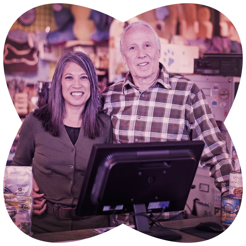 Two people standing in behind computer screen with a blurred indoor background